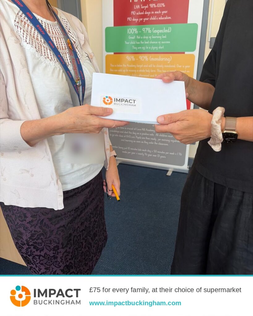 Two people exchange a white box labeled 'Impact Buckingham' in an office setting, with a staff lanyard visible and a promotional poster in the background.